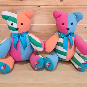 May include: Two colorful handmade teddy bears. One bear is orange, green, blue, and pink with a blue bow. The other bear is pink, blue, orange, and green with a blue bow. Each bear has a lightning bolt design on its foot.