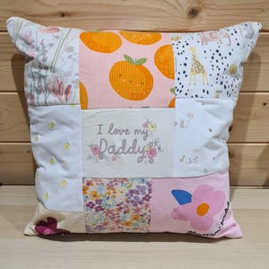 May include: A patchwork pillow with various fabric patterns. The pillow features orange fruit, floral, and animal prints. The center panel reads "I love my Daddy" in script with floral accents. The pillow is square and has a light-colored background.
