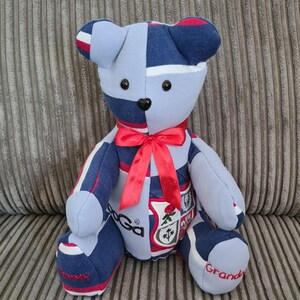 Pu&ograve; includere: Un orsacchiotto a strisce blu e bianche con accenti rossi. L'orso &egrave; fatto di tessuto riutilizzato e ha un fiocco rosso intorno al collo. L'orso ha uno stemma sul petto e le parole "Granda" e "Rugby" sui suoi piedi.