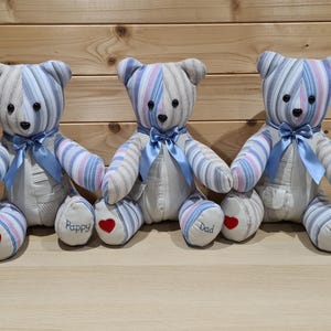 May include: Three handmade teddy bears with striped blue, white, and pink fabric. Each bear has a blue ribbon bow, black button eyes, and a red heart on the foot. One bear has "Dad" embroidered on its foot, and the others say "Pappy".