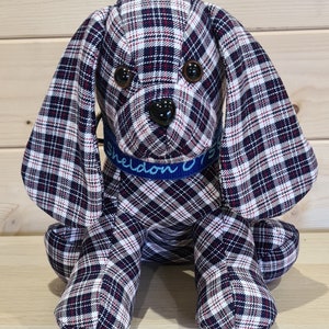 Könnte beinhalten: Ein Plüschtierhund mit einem schwarzen, weißen und roten karierten Muster. Der Hund hat ein blaues Halsband mit dem Namen "Sheldon" darauf gestickt.