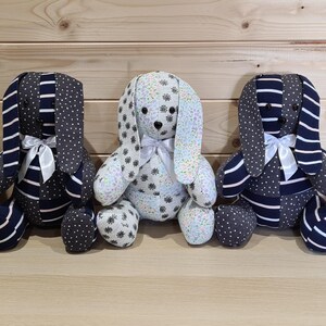 May include: Five handmade plush bunny rabbits with long ears, each with a unique fabric pattern. Some bunnies have white and black polka dot patterns, while others feature navy blue stripes and polka dots. Each bunny has a white satin bow.