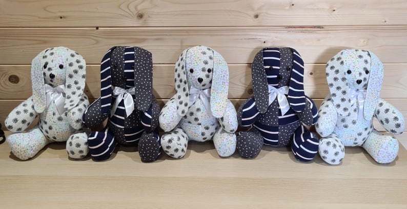 May include: Five handmade plush bunny rabbits with long ears, each with a unique fabric pattern. Some bunnies have white and black polka dot patterns, while others feature navy blue stripes and polka dots. Each bunny has a white satin bow.