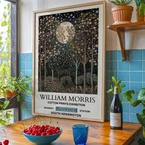 May include: A framed poster with a vintage aesthetic featuring a moonlit forest scene with gold and blue tones. The poster text reads "William Morris Cotton Prints Exhibition Nearest Underground Station South Kensington".