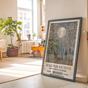 May include: A framed poster with a black frame and a white background. The poster features a black and white illustration of a moonlit forest with the text "William Morris Cotton Prints Exhibition" and "South Kensington" at the bottom.