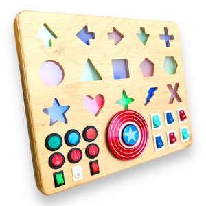 May include: Wooden activity board with various shapes, arrows, and a Captain America shield design. Features colorful toggle switches and buttons. A fun and educational toy for children.