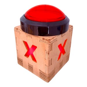 May include: A wooden box with a red, illuminated "X" on two sides, topped with a large, red button. The button has a black base. The box is made of light-colored wood with visible joinery.
