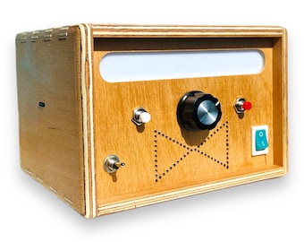May include: A wooden box with a white rectangular opening, a black knob, a white button, a red button, and a green button. The box has a patterned design with a bow tie shape.