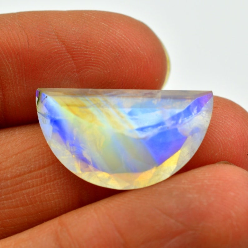 May include: A half-moon shaped iridescent gemstone with a rainbow of colors, including blue, yellow, and white.