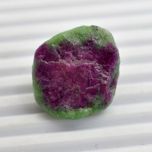 Puede incluir: Una gema áspera, verde y morada con una superficie lisa y pulida.