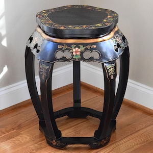 May include: Black, ornate, Asian-style side table with a round top and curved legs. The table features floral and geometric designs in gold, red, and green. The table is made of wood and has a lacquered finish. The table is approximately 18 inches tall.