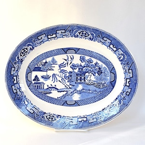 May include: Oval serving platter with a blue and white Willow pattern design. The platter features a detailed landscape scene in the center, surrounded by a decorative border. The blue and white color scheme gives it a classic, vintage look.