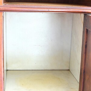 May include: An open wooden cabinet with a light interior. The cabinet has a dark brown exterior and a light-colored interior. The interior has a shelf and a back panel. The cabinet is empty.
