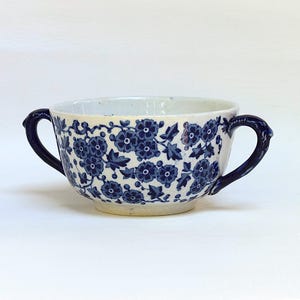 Könnte beinhalten: Eine weiße Suppenschüssel aus Keramik mit blauem Blumenmuster und zwei Henkeln.