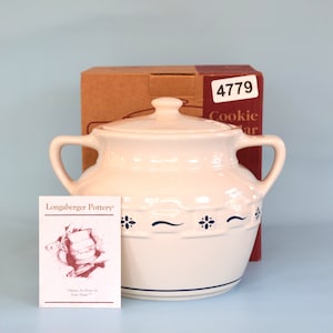 Könnte beinhalten: Eine weiße Keramik-Keksdose mit blauen und weißen Blumenmustern. Die Dose hat einen Deckel und zwei Griffe. Die Dose steht auf einer hellblauen Oberfläche. Die Dose ist mit "Longaberger Pottery" und "4779 Cookie Jar" beschriftet.
