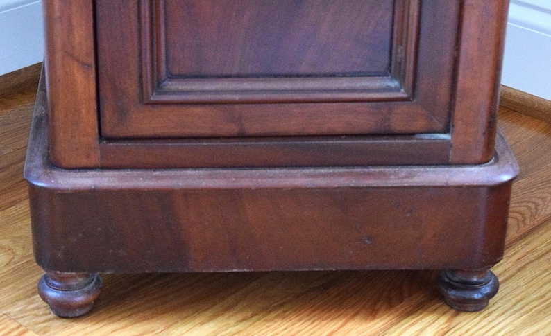 May include: Close-up of a dark brown wooden cabinet base with a rectangular design. The cabinet has a decorative trim and sits on four rounded feet. The wood grain is visible, and the finish appears to be glossy.