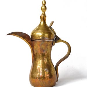 May include: A vintage brass coffee pot with a curved spout, handle, and a decorative finial on the lid. The pot has a warm, aged patina, with areas of golden and reddish-brown tones. The design suggests a Middle Eastern or North African origin.