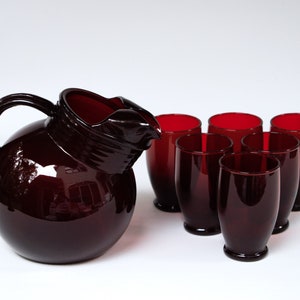 Puede incluir: Un juego de seis vasos de vidrio rojo rubí y una jarra a juego. La jarra tiene un cuerpo redondo y una boca ancha.