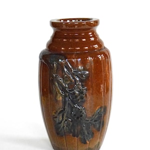 May include: A brown ceramic vase with a raised floral design in black glaze. The vase has a rounded body and a narrow neck.