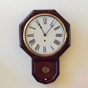 May include: An octagonal wall clock made of dark wood with Roman numeral markings on a white face. The clock has a pendulum and a brass knob.