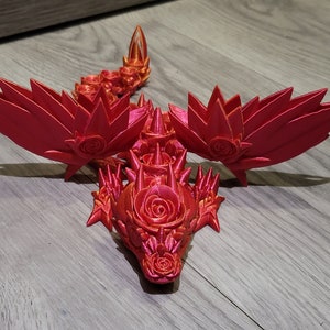 May include: A 3D printed red dragon figurine with rose-shaped details. The dragon has wings and a spiky body.
