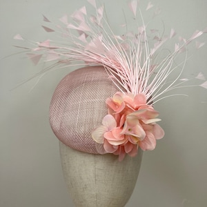 Op de afbeelding: Een roze hoed met een roze bloem en veren.