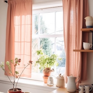 May include: A kitchen window with pink curtains, a potted plant, and a wooden countertop with a variety of kitchenware, including a teapot, mugs, and a coffee maker.