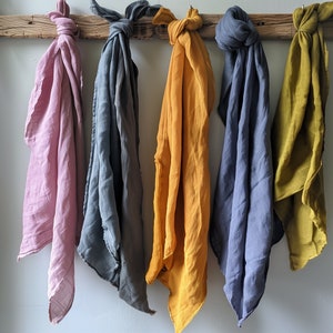 May include: Five fabric squares in different colors hanging from a wooden bar. The squares are pink, gray, yellow, blue, and green.