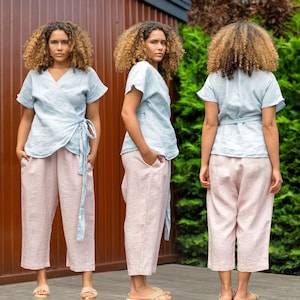 Könnte beinhalten: Ein hellblaues Leinen-Wickeltop mit einer Schleife in der Taille, kombiniert mit einer rosa Leinenhose. Das Model trägt das Top auf drei verschiedene Arten und zeigt so die Vielseitigkeit des Kleidungsstücks.