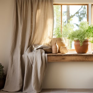 K&ouml;nnte beinhalten: Ein Fenster mit einer Holzbank und einem beigefarbenen Leinenvorhang. Das Fenster ist mit Topfpflanzen, einem geflochtenen Korb und einer Terrakottavase dekoriert.
