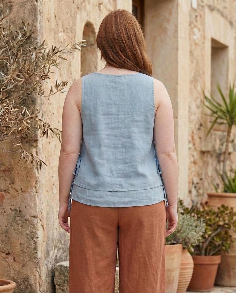 Puede incluir: Una blusa sin mangas azul claro con un dise&ntilde;o en capas y detalles de lazo, combinada con pantalones de pierna ancha color &oacute;xido. El conjunto est&aacute; hecho de tela tipo lino, lo que sugiere un estilo casual y c&oacute;modo. El modelo est&aacute; al aire libre.