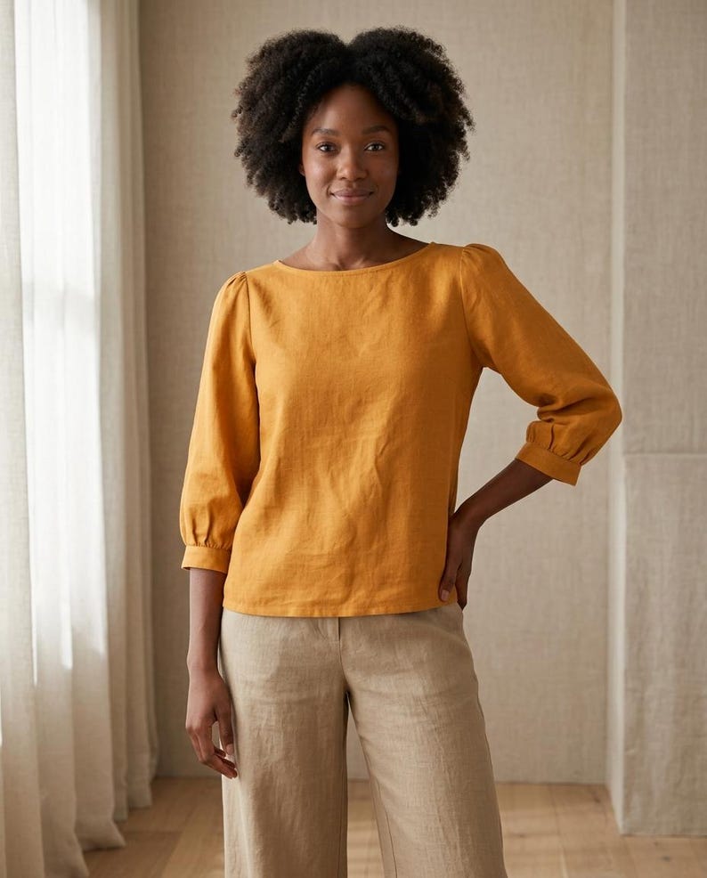 May include: A mustard yellow long-sleeved blouse with a boat neckline and gathered puff sleeves, paired with light beige wide-leg trousers. The blouse features a straight hemline and cuffed sleeves, while the trousers have a simple waistband.