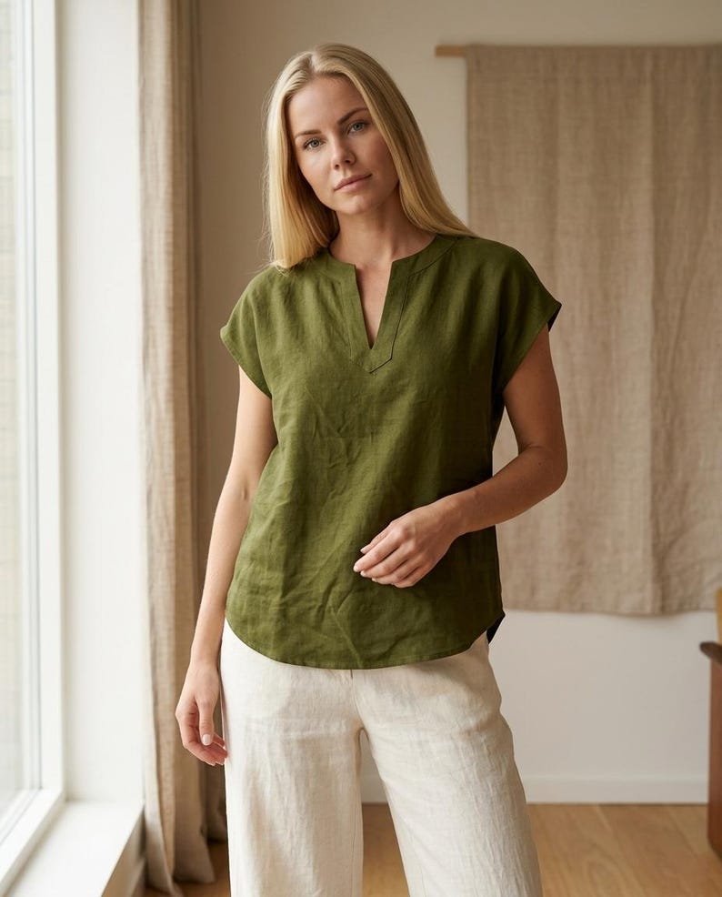May include: An olive green short-sleeved blouse featuring a notched neckline and a relaxed fit. The top is constructed from a textured fabric and is paired with light beige trousers that have a straight-leg cut and a clean, simple design.