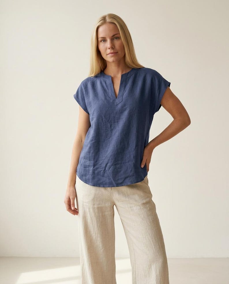 May include: A short-sleeved navy blue blouse featuring a notched neckline and a relaxed fit, paired with wide-leg beige trousers. The blouse has a straight hemline and the trousers have a loose, flowing silhouette with a neutral, light tan color.