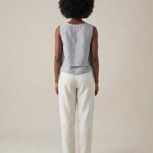 Puede incluir: Un top sin mangas gris claro con un dise&ntilde;o en capas y pantalones de lino blanco roto a juego. El top tiene un cuello redondo y los pantalones tienen un corte relajado. El conjunto est&aacute; hecho de una tela ligera, perfecto para el clima c&aacute;lido.