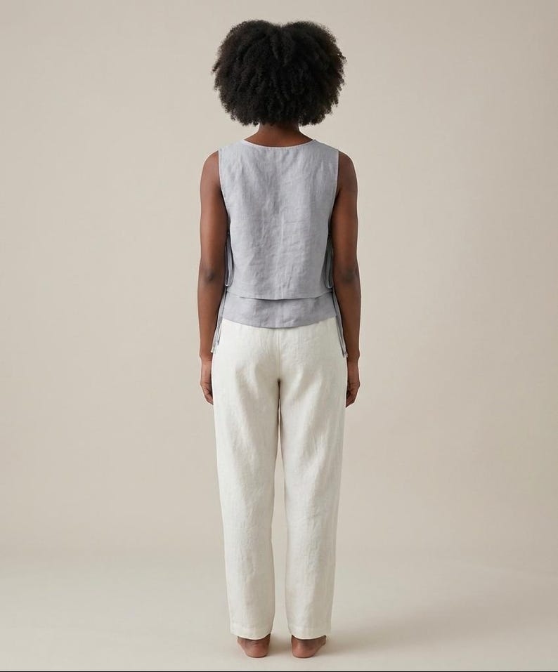 Puede incluir: Un top sin mangas gris claro con un dise&ntilde;o en capas y pantalones de lino blanco roto a juego. El top tiene un cuello redondo y los pantalones tienen un corte relajado. El conjunto est&aacute; hecho de una tela ligera, perfecto para el clima c&aacute;lido.