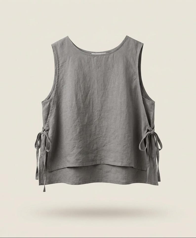 Puede incluir: Una blusa sin mangas de lino gris con cuello redondo y lazos laterales. La blusa tiene un dise&ntilde;o en capas y un ajuste relajado. La tela parece suave y ligeramente texturizada.