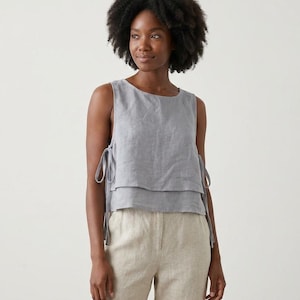 Puede incluir: Top sin mangas gris claro con dise&ntilde;o en capas y lazos laterales. Combinado con pantalones de lino beige claro. El conjunto es de lino, ideal para un estilo casual y veraniego.