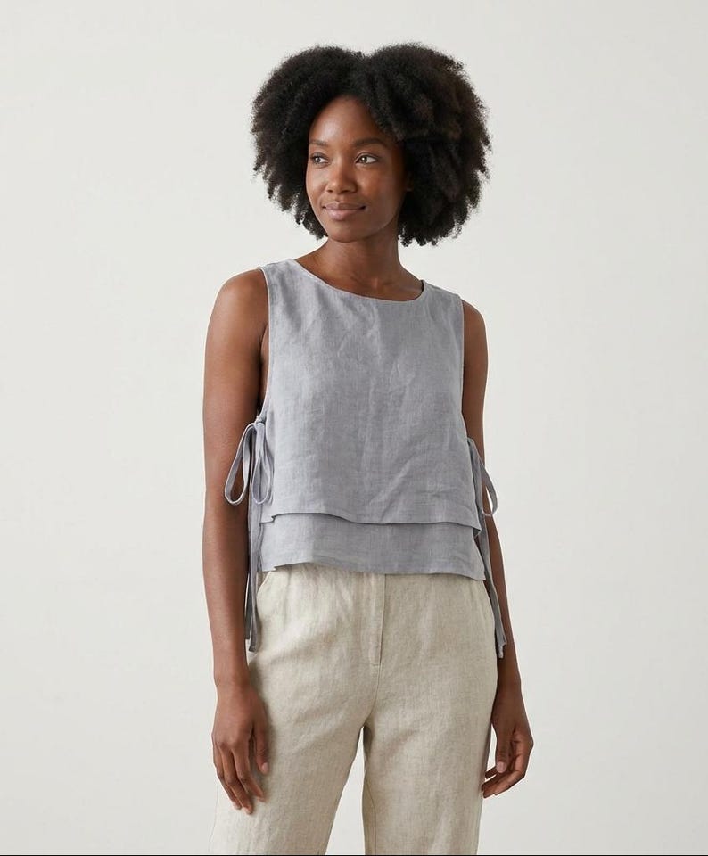 Puede incluir: Top sin mangas gris claro con dise&ntilde;o en capas y lazos laterales. Combinado con pantalones de lino beige claro. El conjunto es de lino, ideal para un estilo casual y veraniego.