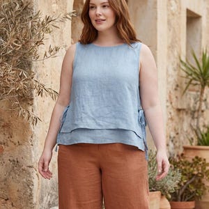 Puede incluir: Un top sin mangas de lino azul claro con detalles de lazo en los laterales, combinado con pantalones de lino color &oacute;xido. El conjunto es sencillo y elegante. El top tiene un dise&ntilde;o en capas.