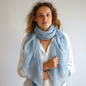 May include: A light blue linen scarf draped around a person's neck. The scarf is made of a soft, lightweight fabric and has a simple, elegant design.