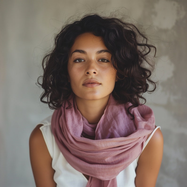 May include: A woman with curly brown hair wearing a pink scarf. She is looking directly at the camera.