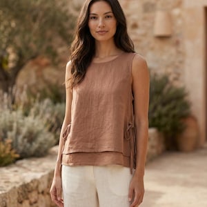 Puede incluir: Un top sin mangas de color marr&oacute;n c&aacute;lido con dise&ntilde;o en capas y lazos laterales. Se combina con pantalones de pierna ancha color crema. El conjunto est&aacute; hecho de una tela ligera, ideal para el clima c&aacute;lido. El top tiene un cuello redondo y un corte holgado.