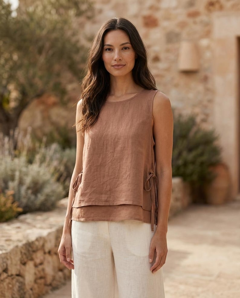 Puede incluir: Un top sin mangas de color marr&oacute;n c&aacute;lido con dise&ntilde;o en capas y lazos laterales. Se combina con pantalones de pierna ancha color crema. El conjunto est&aacute; hecho de una tela ligera, ideal para el clima c&aacute;lido. El top tiene un cuello redondo y un corte holgado.