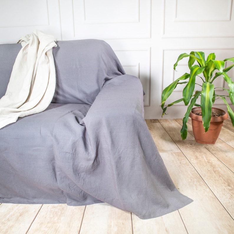 a couch covered in a linen couch cover next to a potted plant