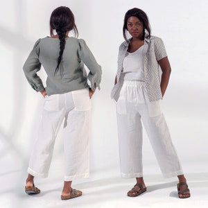 Pu&ograve; includere: Due donne indossano pantaloni di lino bianchi. La donna a sinistra indossa una camicetta di lino verde. La donna a destra indossa una camicetta bianca e una camicia a quadri bianchi e neri. Entrambe le donne indossano sandali.