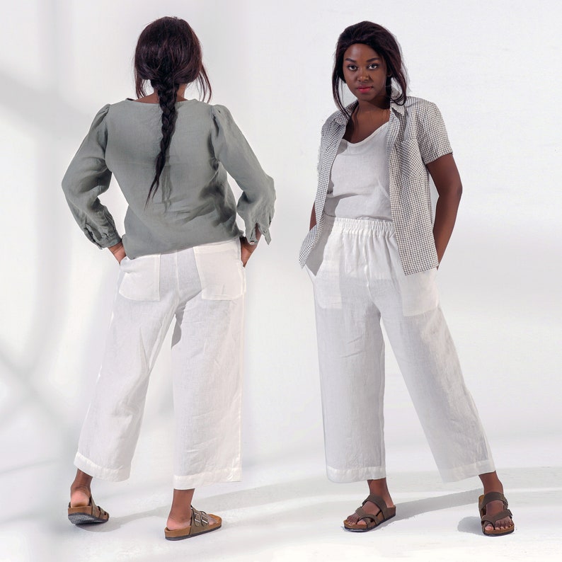 Pu&ograve; includere: Due donne indossano pantaloni di lino bianchi. La donna a sinistra indossa una camicetta di lino verde. La donna a destra indossa una camicetta bianca e una camicia a quadri bianchi e neri. Entrambe le donne indossano sandali.