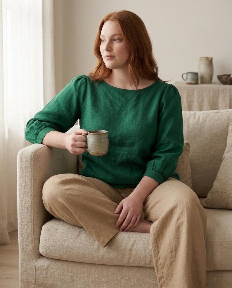 May include: A long-sleeved emerald green linen blouse with a round neckline and gathered cuffs, paired with loose-fitting tan linen trousers. The blouse features a simple, solid-colored design with a relaxed fit, while the trousers have a wide-leg cut.