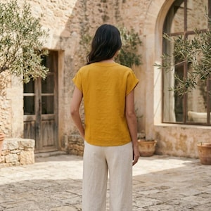 May include: A mustard yellow short-sleeved top with a round neckline paired with light beige wide-leg trousers. The top features a simple, solid-colored design with short sleeves, while the trousers have a loose, straight-leg fit.