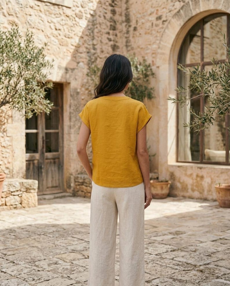 May include: A mustard yellow short-sleeved top with a round neckline paired with light beige wide-leg trousers. The top features a simple, solid-colored design with short sleeves, while the trousers have a loose, straight-leg fit.